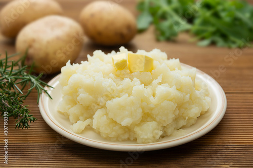 Mashed potatoes with butter and fresh white potatoes on background, wooden table. Healthy food for kids, dinner.