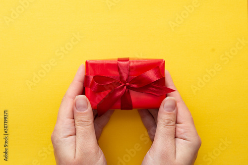 Fototapeta Naklejka Na Ścianę i Meble -  Top view of female hands holding gift red box with ribbon bow isolated over blue background, copy space.
