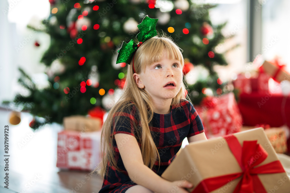 Young girl sitting on the floor holding present thinking Young girl sitting on the floor holding present thinking