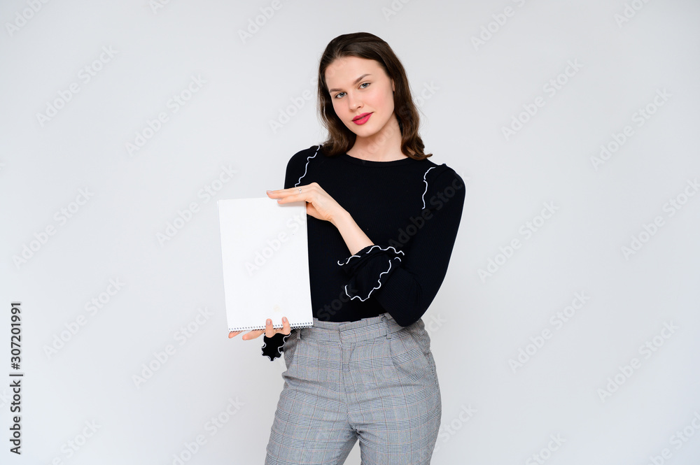 Concept adult girl on a white background with a white folder in hands. A photo of a pretty brunette girl in gray trousers and a black sweater smiles and shows different emotions in different poses. Concept adult girl on a white background with a white folder in hands. A photo of a pretty brunette girl in gray trousers and a black sweater smiles and shows different emotions in different poses.