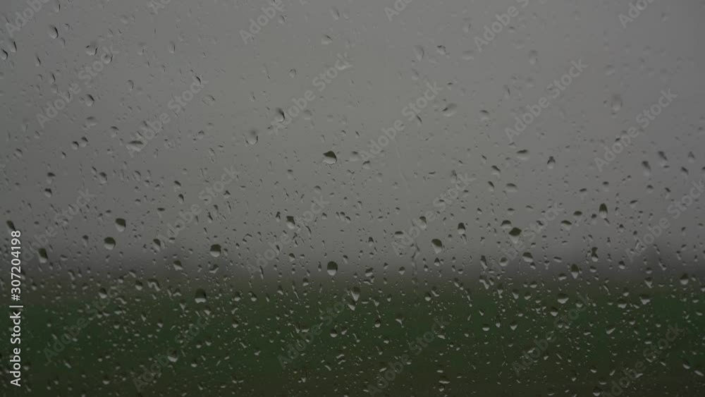 heavy rain drops fall on transparent glass and run down against blurry green field silhouette slow motion close view heavy rain drops fall on transparent glass and run down against blurry green field silhouette slow motion close view