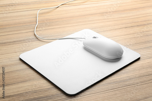 Modern wired optical mouse and pad on wooden table photo