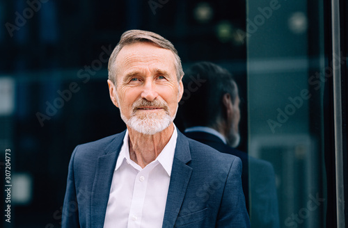 Portrait of a bearded businessman standing at glass front and looking away