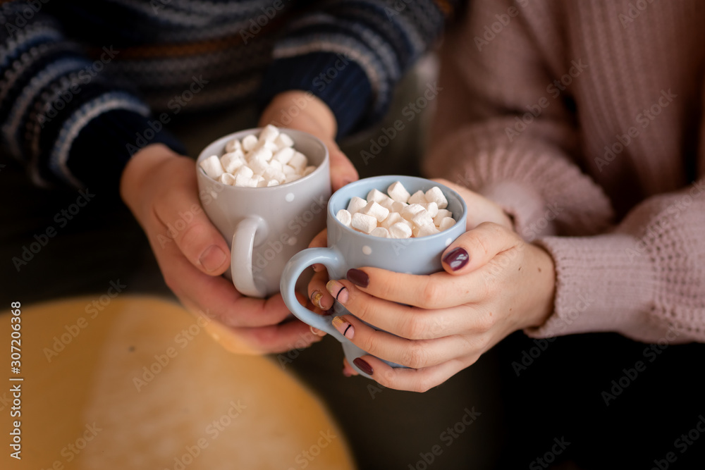 Happy couple's hands holding hot cups with hot drinks with marshmallow.
