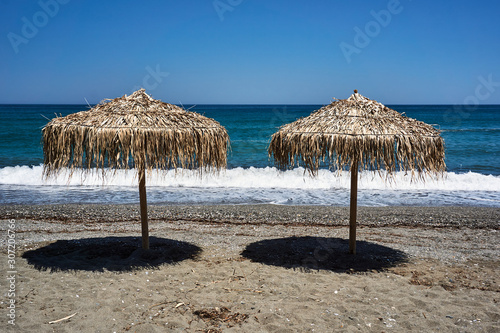 Beach umbrellas made of palm leaves on the beach of the Aegean Sea in Greece.