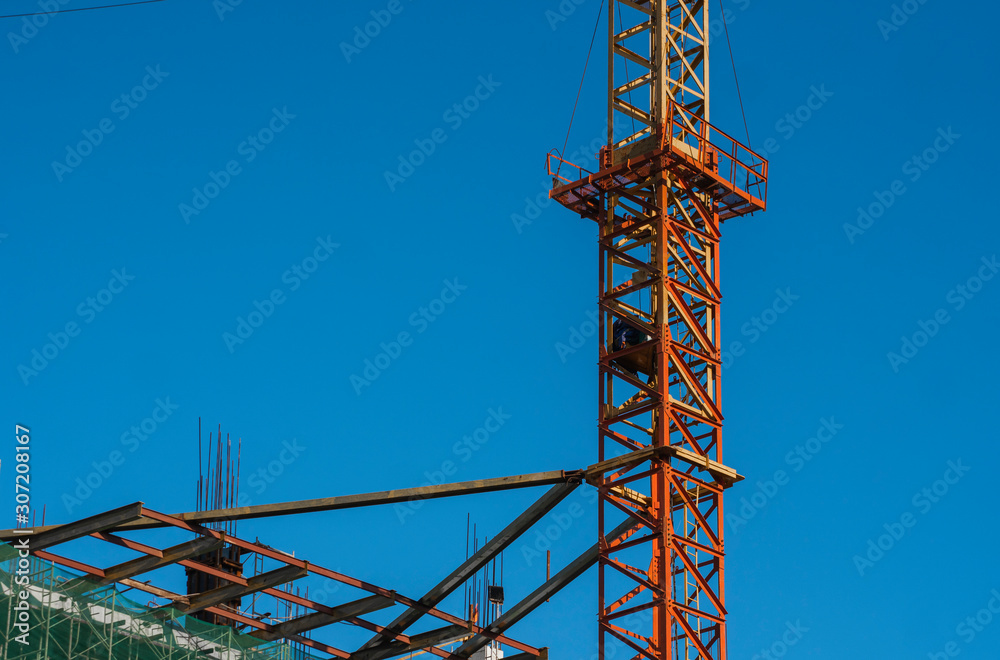 Crane and building construction site against blue sky. Metal construction of unfinished building on construction. Tower Crane use for building of multi storage building.