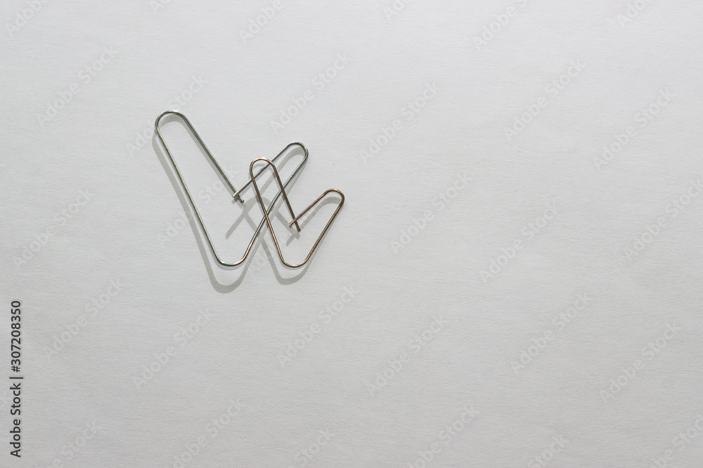 Two metal paper clips in the form of two checkmarks on a white paper sheet. Two hearts made of paper clips on a white background. Paper texture. Two metal paper clips in the form of two checkmarks on a white paper sheet. Two hearts made of paper clips on a white background. Paper texture.