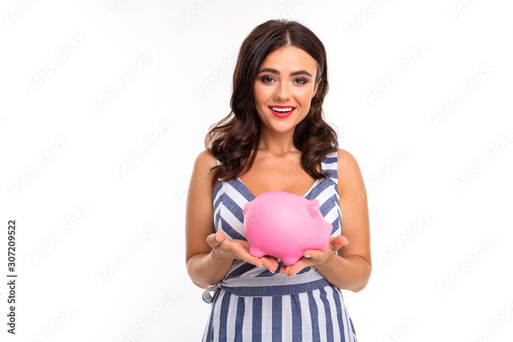 European attractive brunette in dress holds a piggy bank in her hands on a white studio background European attractive brunette in dress holds a piggy bank in her hands on a white studio background