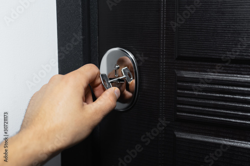 Close-up of male hand unlocking or locking lock of modern house door with key.