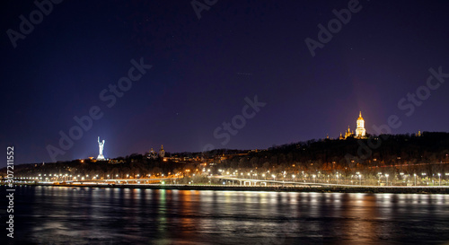 Beautiful night city of Kiev and the Dnieper river in the foreground with illumination of the embankment with a long exposure, Kiev, Ukraine