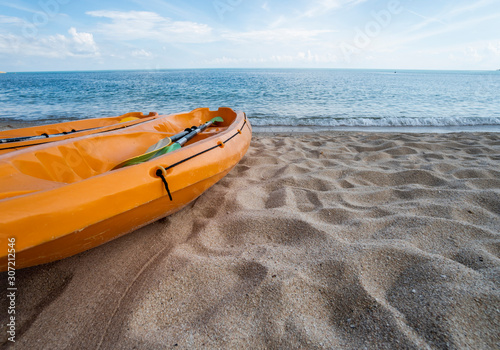 Two colorful orange kayaks on a sandy beach ready for paddlers in sunny day. Several orange recreational boats on the sand. Active tourism and water recreation.