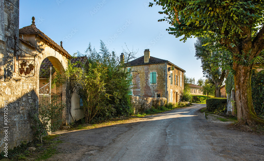 village street in France with stone houses, road and trees