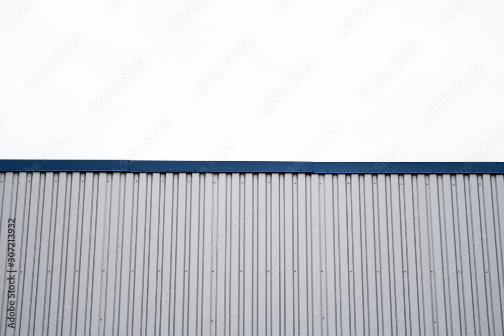 Metal corrugated sheets on a building with a blue metal corners. White aluminium metal corrugated roof or wall sheets against cloudy sky background on a factories and industrial buildings. Metal corrugated sheets on a building with a blue metal corners. White aluminium metal corrugated roof or wall sheets against cloudy sky background on a factories and industrial buildings.