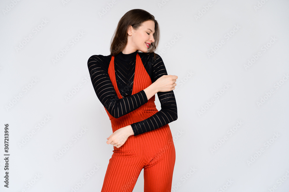 Concept adult girl on a white background. A photo of a pretty brunette girl in red trousers and a black sweater smiles and shows different emotions in different poses right in front of the camera. Concept adult girl on a white background. A photo of a pretty brunette girl in red trousers and a black sweater smiles and shows different emotions in different poses right in front of the camera.