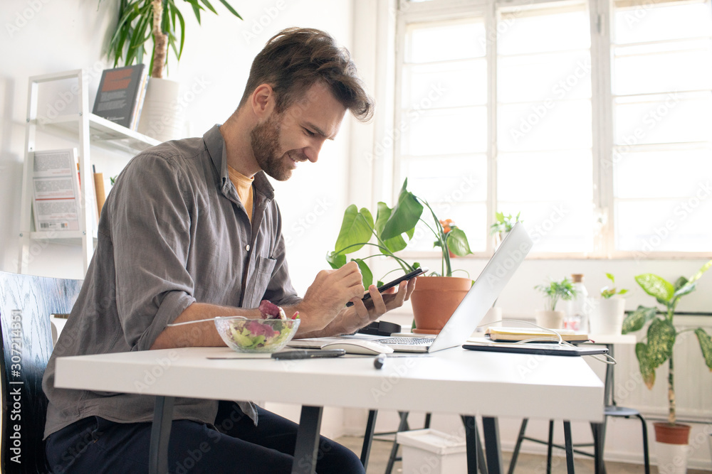 Smiling man using smartphone during lunch break at desk in office