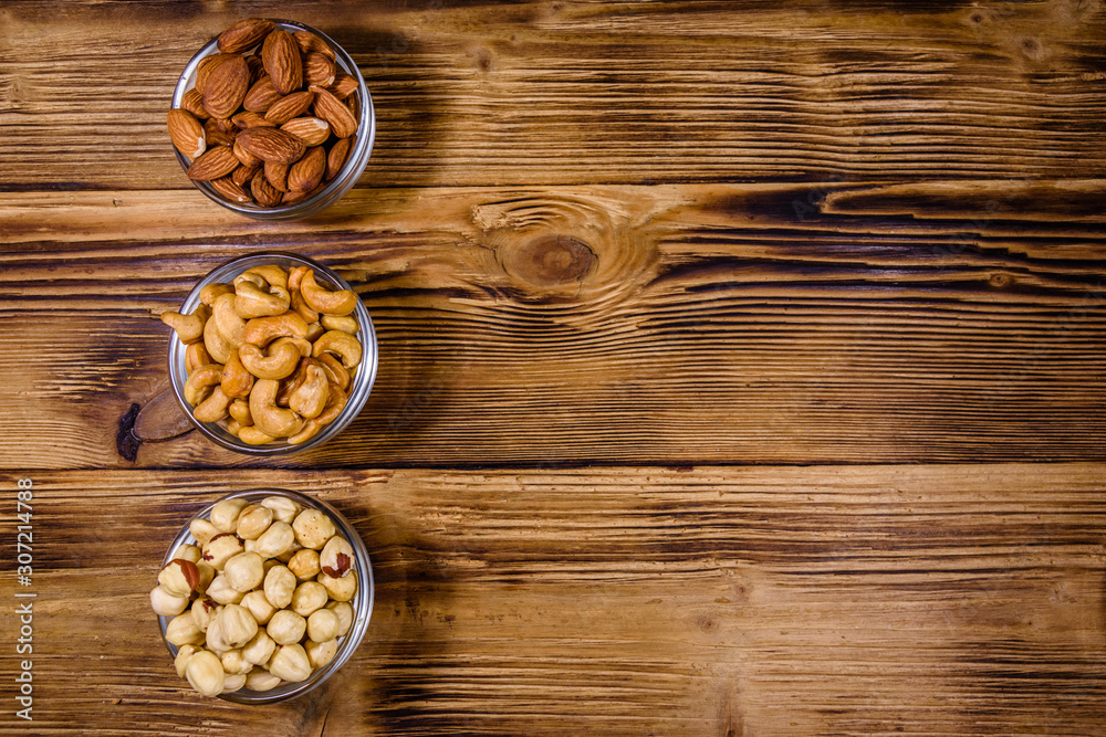 Various nuts (almond, cashew, hazelnut) in glass bowls on a wooden table. Vegetarian meal. Healthy eating concept. Top view Various nuts (almond, cashew, hazelnut) in glass bowls on a wooden table. Vegetarian meal. Healthy eating concept. Top view