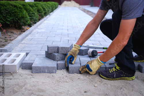 The master in yellow gloves lays paving stones