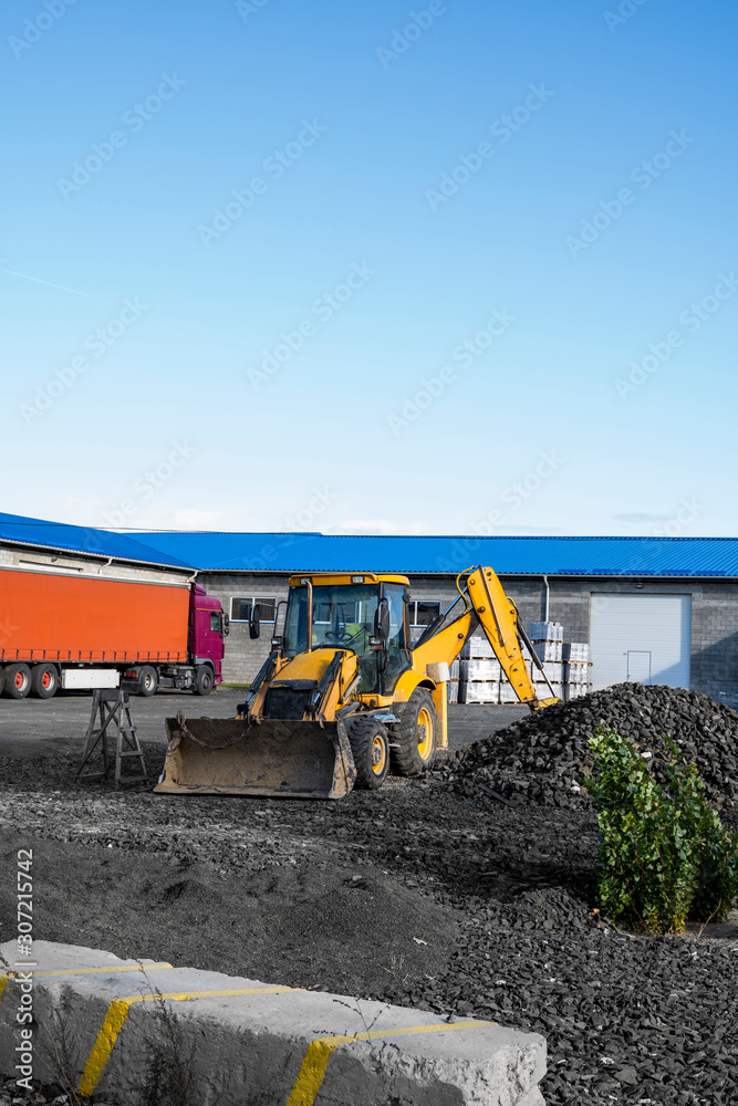 Obraz premium The yellow all-wheel drive backhoe loader stands on the yard ready for workind on construction site.
