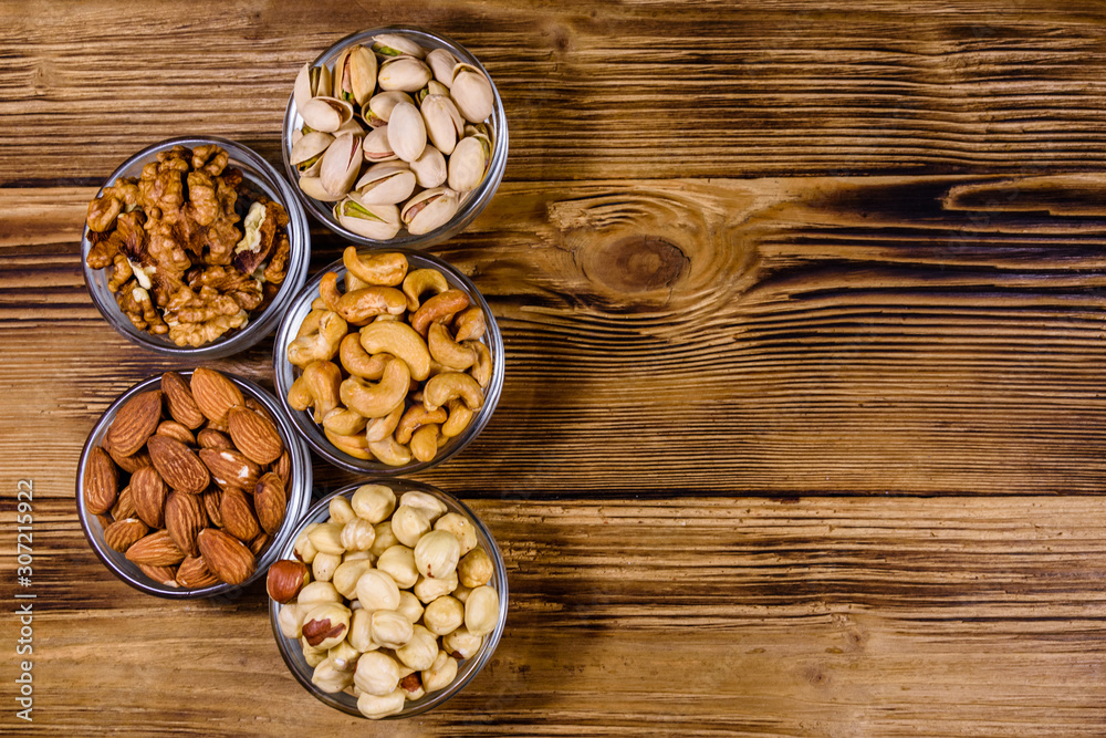 Various nuts (almond, cashew, hazelnut, pistachio, walnut) in glass bowls on a wooden table. Vegetarian meal. Healthy eating concept. Top view Various nuts (almond, cashew, hazelnut, pistachio, walnut) in glass bowls on a wooden table. Vegetarian meal. Healthy eating concept. Top view
