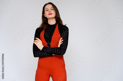 Concept adult girl on a white background. A photo of a pretty brunette girl in red trousers and a black sweater smiles and shows different emotions in different poses right in front of the camera.