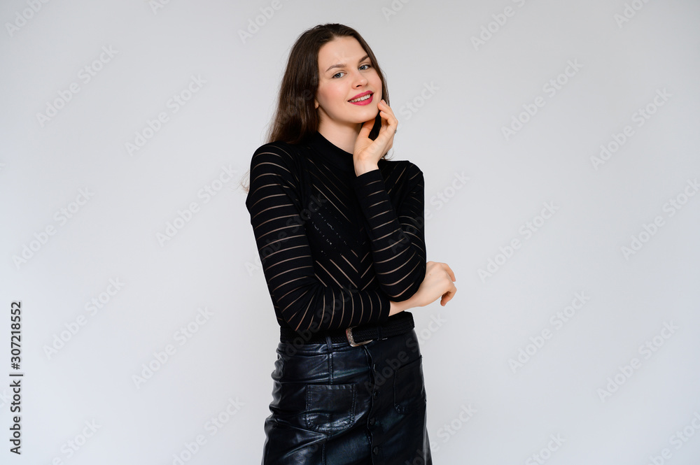 Concept adult girl on a white background. A photo of a pretty brunette girl in a black skirt and black sweater smiles and shows different emotions in different poses right in front of the camera. Concept adult girl on a white background. A photo of a pretty brunette girl in a black skirt and black sweater smiles and shows different emotions in different poses right in front of the camera.