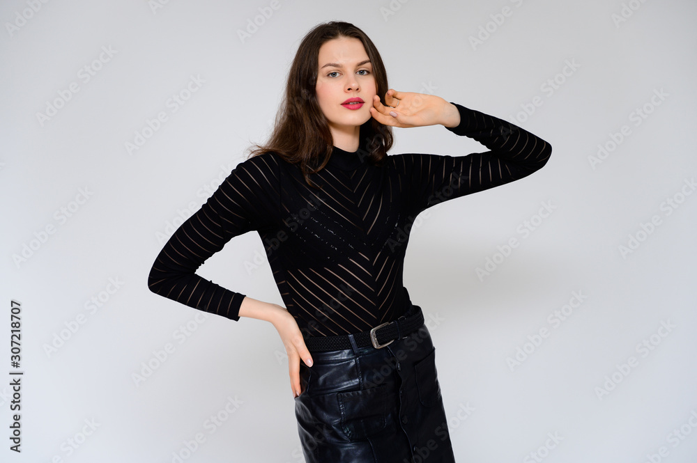 Concept adult girl on a white background. A photo of a pretty brunette girl in a black skirt and black sweater smiles and shows different emotions in different poses right in front of the camera. Concept adult girl on a white background. A photo of a pretty brunette girl in a black skirt and black sweater smiles and shows different emotions in different poses right in front of the camera.