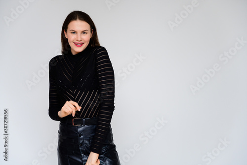 Concept adult girl on a white background. A photo of a pretty brunette girl in a black skirt and black sweater smiles and shows different emotions in different poses right in front of the camera. © Вячеслав Чичаев