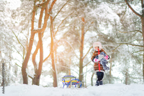 Cute girl plays in the winter forest at sunset. Children sledding in a snowy park. Winter holiday.