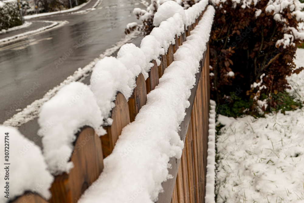 Wooden fence with snowy crowns on the muddy road