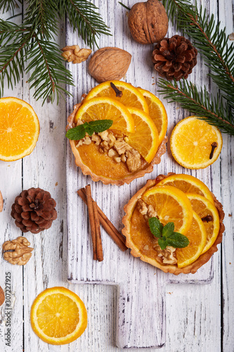 Mini tart pies with orange, custard cream and walnuts on wooden background. Sweet Christmas dessert. 