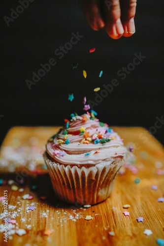 Person putting sprinkles on cupcake photo