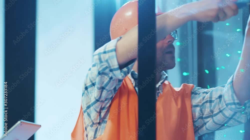 Team of data center electrical technicians coworking in server cabinet. Two multi-ethnic engineers repairing electric components on server racks at database.