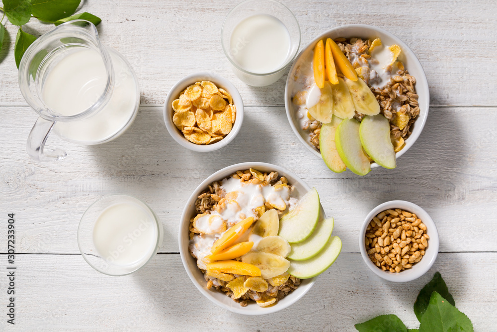 Bowls with granola, fruit, yogurt and two glasses with milk on a white wooden background. Healthy breakfast cereal Bowls with granola, fruit, yogurt and two glasses with milk on a white wooden background. Healthy breakfast cereal