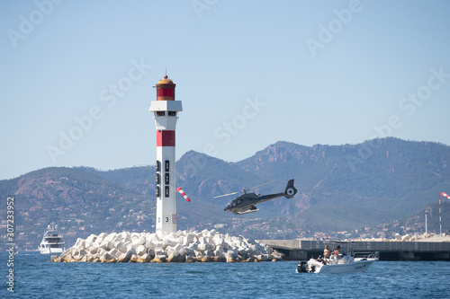 Thrilling View: Helicopter Flying Low Behind Lighthouse at Cannes Port © SPIX PRODUCTION