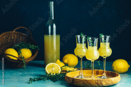 Limoncello with thyme in three grappas wineglass in wooden tray, fresh lemon in basket. Artistic still life on dark blue background photo