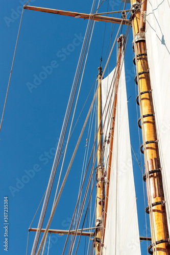 Vertical low angle closeup shot of the sails of a schooner on blue background
