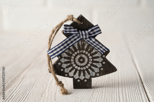 Wooden Christmas tree with a blue bow with an image of a white snowflake on a white natural wooden background.