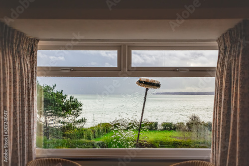 Fototapeta A double glazed picture window with small top light opening windows being cleaned with an extension brush and pure water. Some motion blur showing the movement of the brush. There is a sea view.