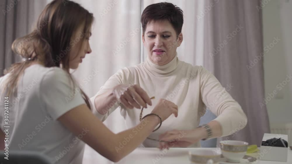 Portrait of mature Caucasian woman presenting bracelet to daughter. Mother giving jewelry to young beautiful girl. Care, gift, good relationship, happiness. Portrait of mature Caucasian woman presenting bracelet to daughter. Mother giving jewelry to young beautiful girl. Care, gift, good relationship, happiness.
