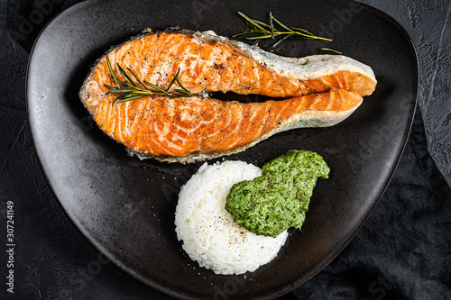 Grilled salmon steak garnished with rice and spinach. Black background. Top view