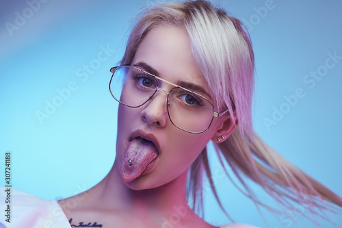 Canvas Print Closeup portrait of a cocky blonde girl wearing glasses poses with tongue sticking out looking at the camera