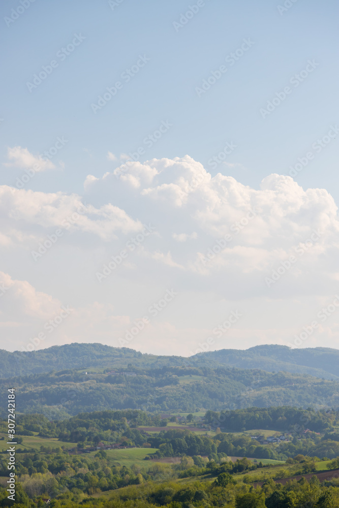 hilly landscape rich in tree vegetation with some houses and cloudy blue sky hilly landscape rich in tree vegetation with some houses and cloudy blue sky