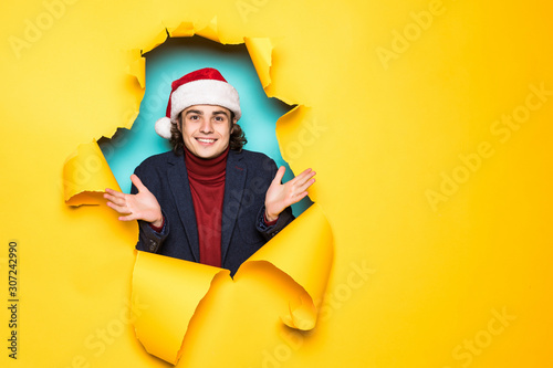 Young man in santa hat with reised hands through yellow paper hole. Christmas sales. © F8  \ Suport Ukraine