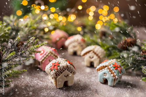 Gingerbread house on the background of a Christmas tree and a lie garland. Handling the effect of snowfall.