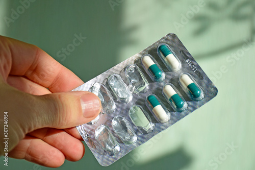Hand man holds foil packet of pills. Green tablets packed in blister.  Healthcare and medicine concept, flu season