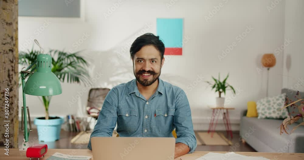 Pleasant man smiling showing finger up gesture in inspiration moment of new big idea, bearded Hispanic male working behind desk at home dressed in blue jeans shirt, business startup content indoor Pleasant man smiling showing finger up gesture in inspiration moment of new big idea, bearded Hispanic male working behind desk at home dressed in blue jeans shirt, business startup content indoor