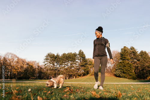Fotografie Happy black sportswoman walking with her dog at the park.