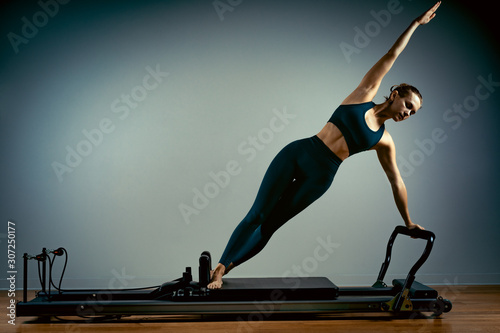 Foto Young girl doing pilates exercises with a reformer bed