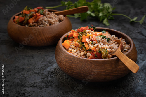 Vegan buckwheat groats cooked with carrot and roasted bellpepper served in wooden bowls