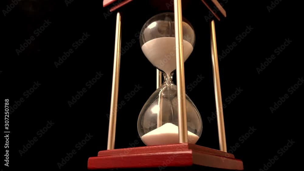 Hourglass on a stand, black background. Glass hourglass in the case. Glass time meter. Concept: time is running out, time management, time resource